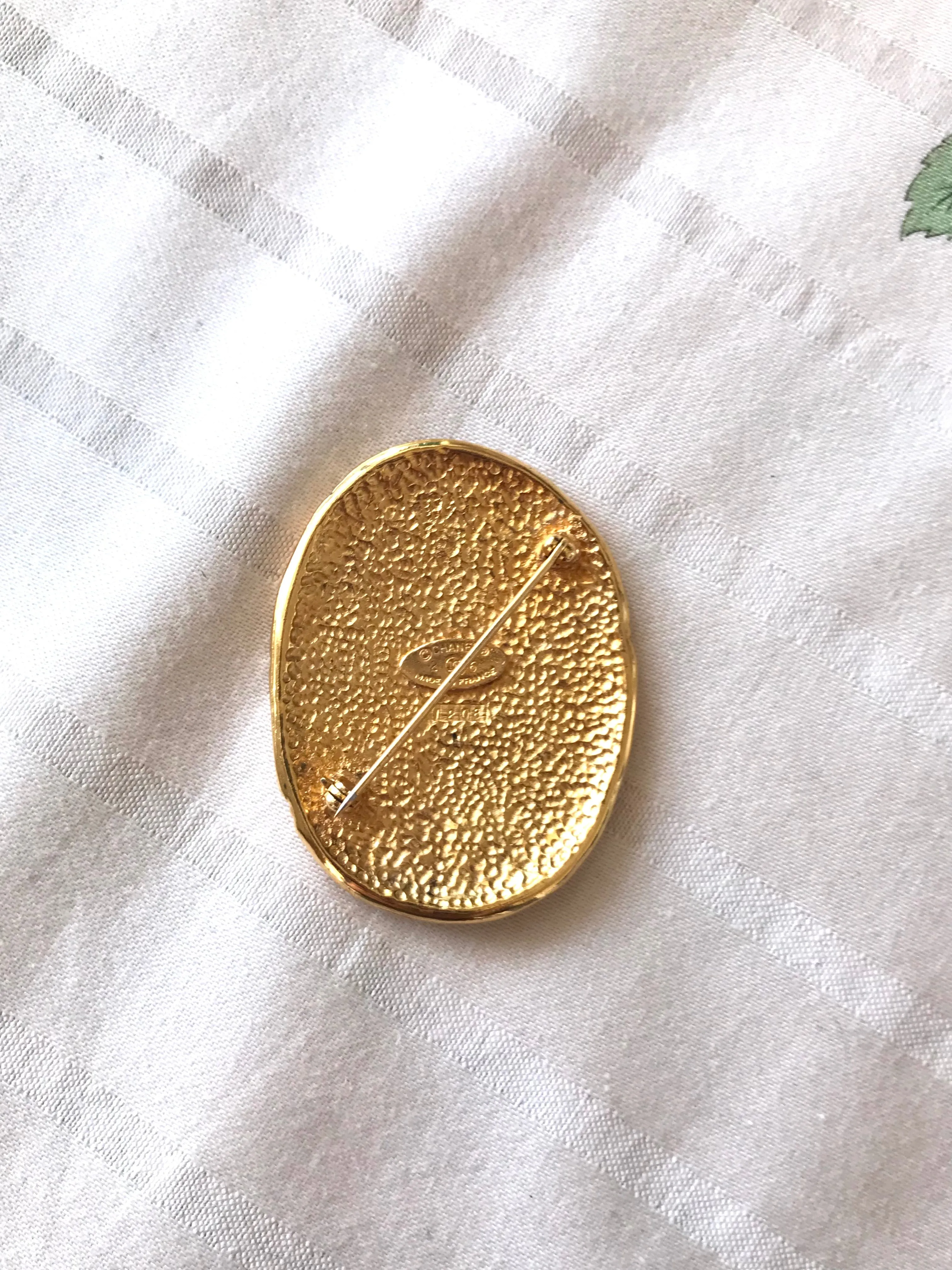 Vintage CHANEL gold tone large brooch in oval coin shape with CC logo and crown embossed motif. Rare masterpiece jewelry. 060620re3